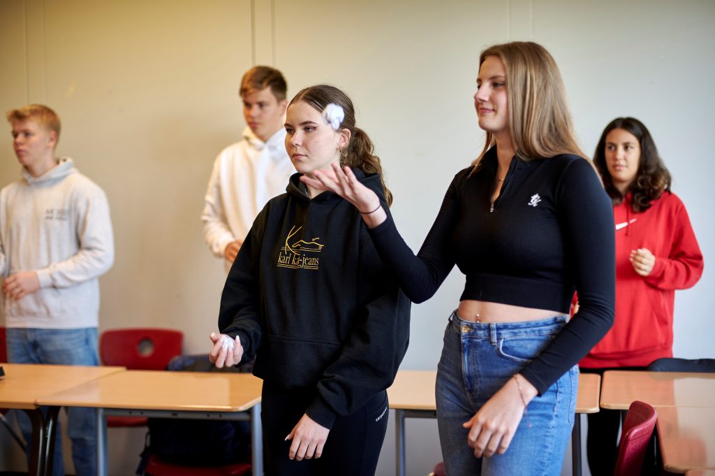 Jugendliche stehen im Klassenzimmer und werfen Kugeln aus zerknülltem Papier in die Luft.
